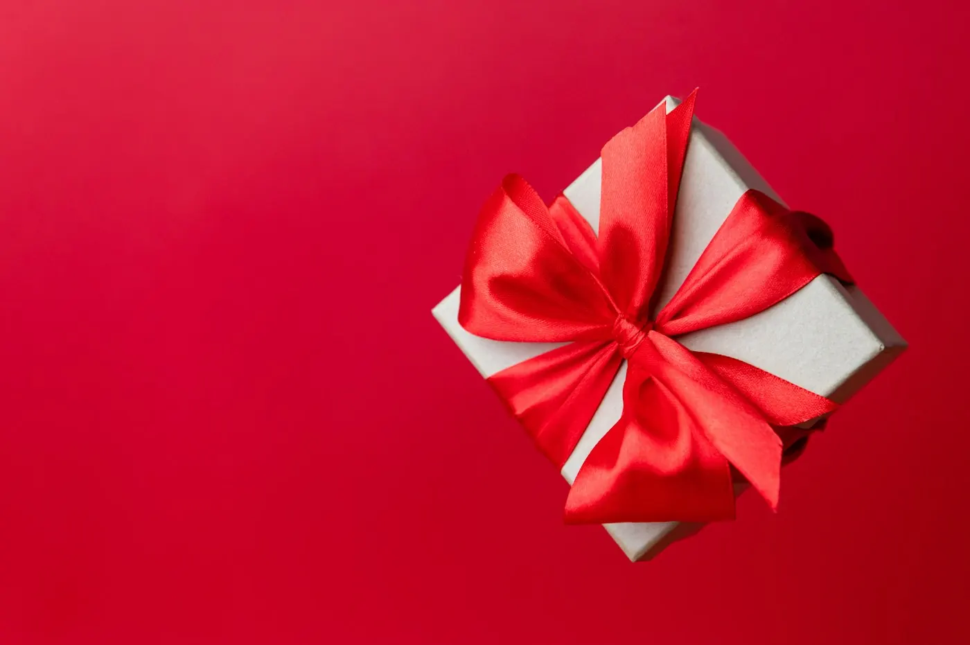 White gift box tied with a red ribbon on a red background